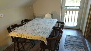 A dining area with a table covered by a floral tablecloth, surrounded by wooden chairs, a radiator, and a view through a glass door. - Room-small Village, Small Guest House, w (Dunaszentmiklós)