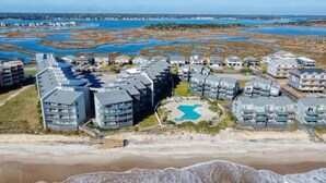 A coastal residential area with modern apartment buildings, a swimming pool, and a beach in the foreground. - Oceanfront North Topsail Beach Condo w/Pool! Linens and towels provided (North Topsail Beach)