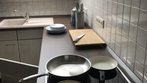A kitchen with a stove, pots, a knife block, and a window. - Wooden Roof, 95 qm, 5 Pers (Attendorn)