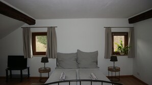 A bedroom with a bed, two bedside tables, a TV, and windows with curtains. - Wooden Roof, 95 qm, 5 Pers (Attendorn)