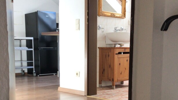 A spacious room with a wooden floor, a kitchen area with a sink and cabinets, and a large mirror on the wall. - Wooden Roof, 95 qm, 5 Pers (Attendorn)