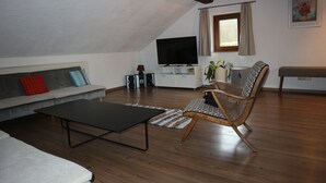 A modern living room with a flat-screen TV, a sofa, a coffee table, and a wicker chair. - Wooden Roof, 95 qm, 5 Pers (Attendorn)