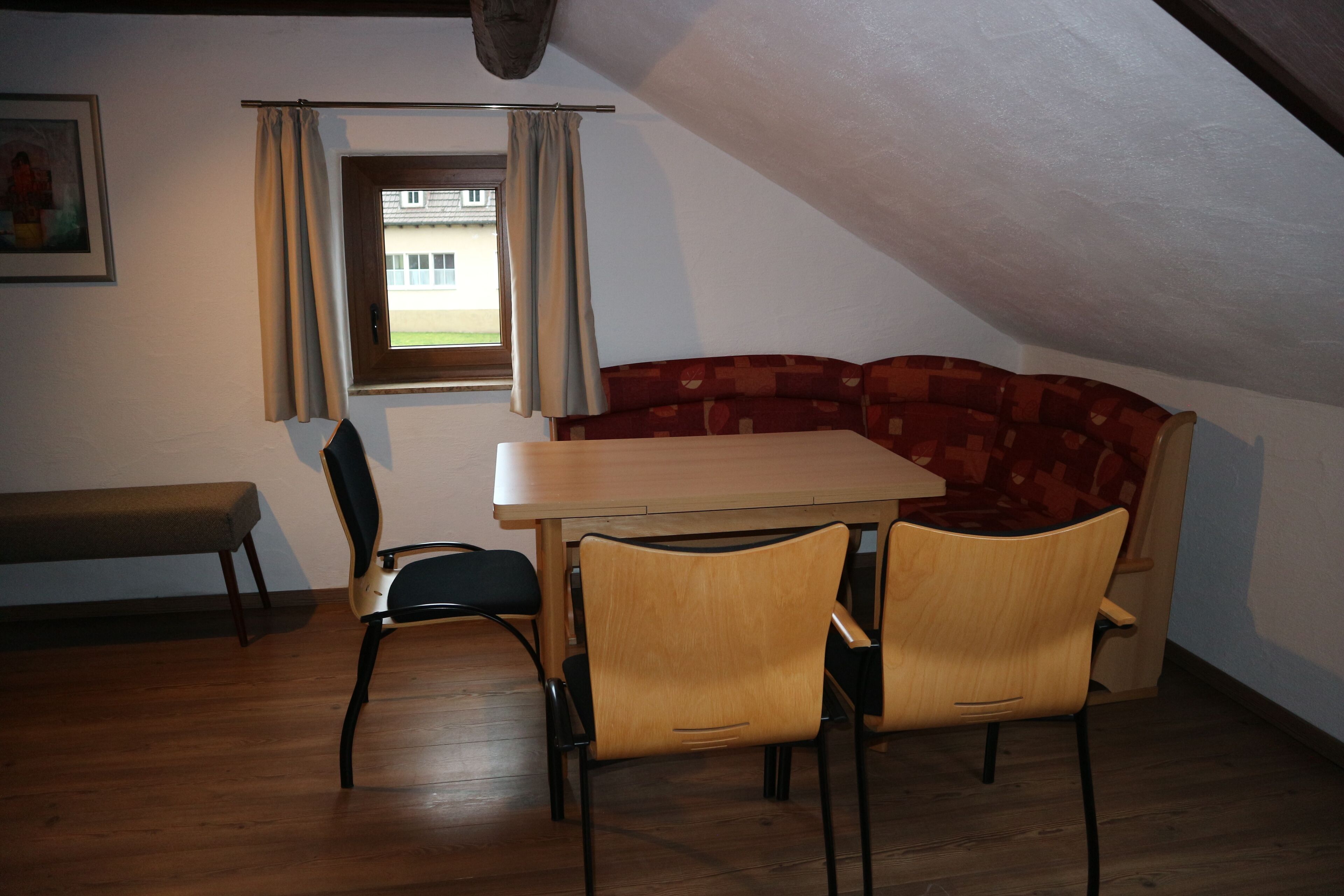 Un coin repas avec une table et des chaises en bois, un banc et une fenêtre avec des rideaux.