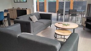 Un saló modern amb un sofà gris, una taula de cafè de fusta i una zona de menjador amb una taula i cadires de fusta.