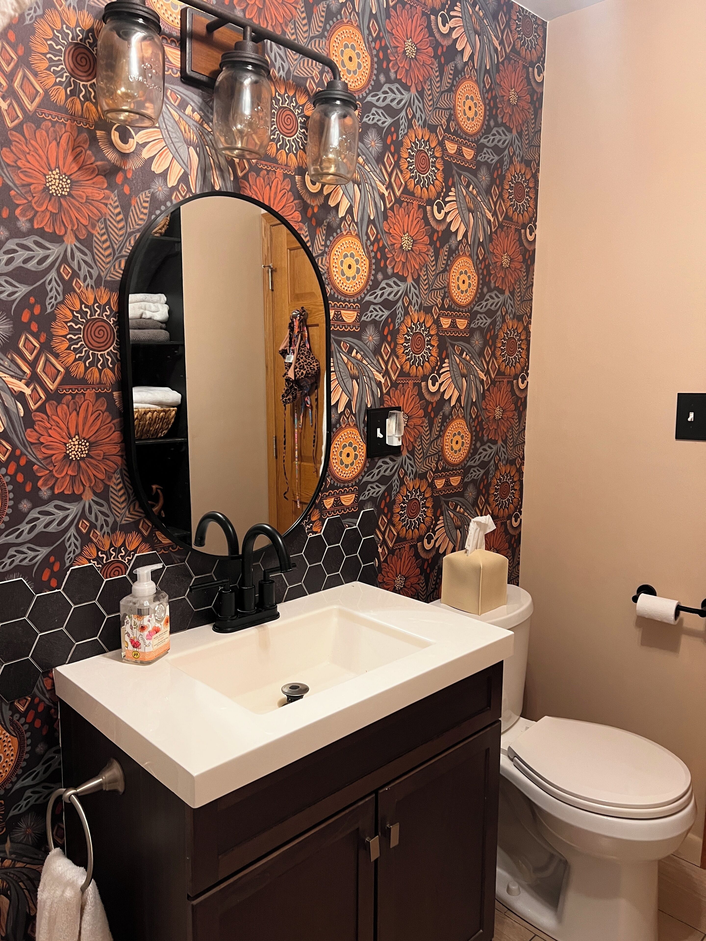 A bathroom with a patterned wall, a sink with a soap dispenser, a toilet, and a mirror.