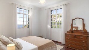 Un dormitorio con cama, cómoda y dos ventanas con cortinas.