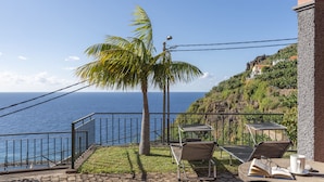 Un patio con vista al océano, una palmera, y una mesa con sillas y un libro.