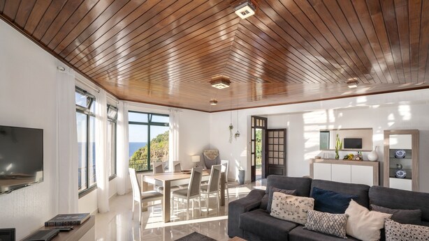 Una sala de estar moderna con techo de madera, un sofá gris, un comedor y un televisor montado en la pared.