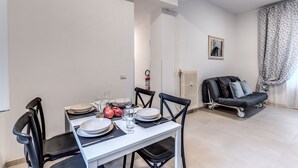 A dining area with a white table set for four, black chairs, and a black sofa in the background. - PMT APT (Rome)