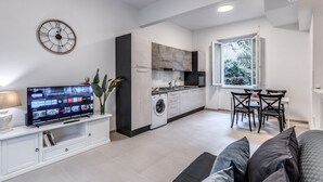 A modern kitchen with a built-in washer and dryer, a dining area with a table and chairs, and a large flat-screen TV mounted on a white cabinet. - PMT APT (Rome)