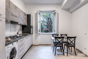 Een moderne keuken met een ingebouwde oven, een wasmachine en een eethoek met een tafel en stoelen.