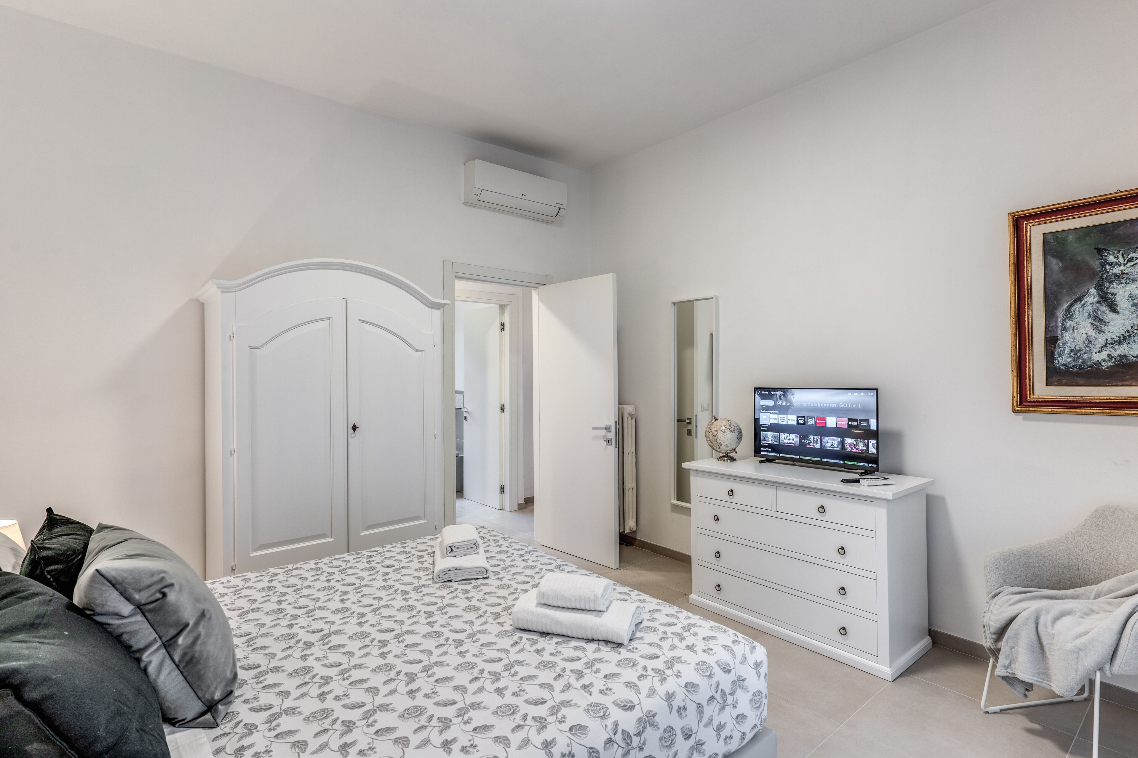 Een slaapkamer met een bed, een dressoir, een televisietoestel en een ingelijste foto aan de muur.
