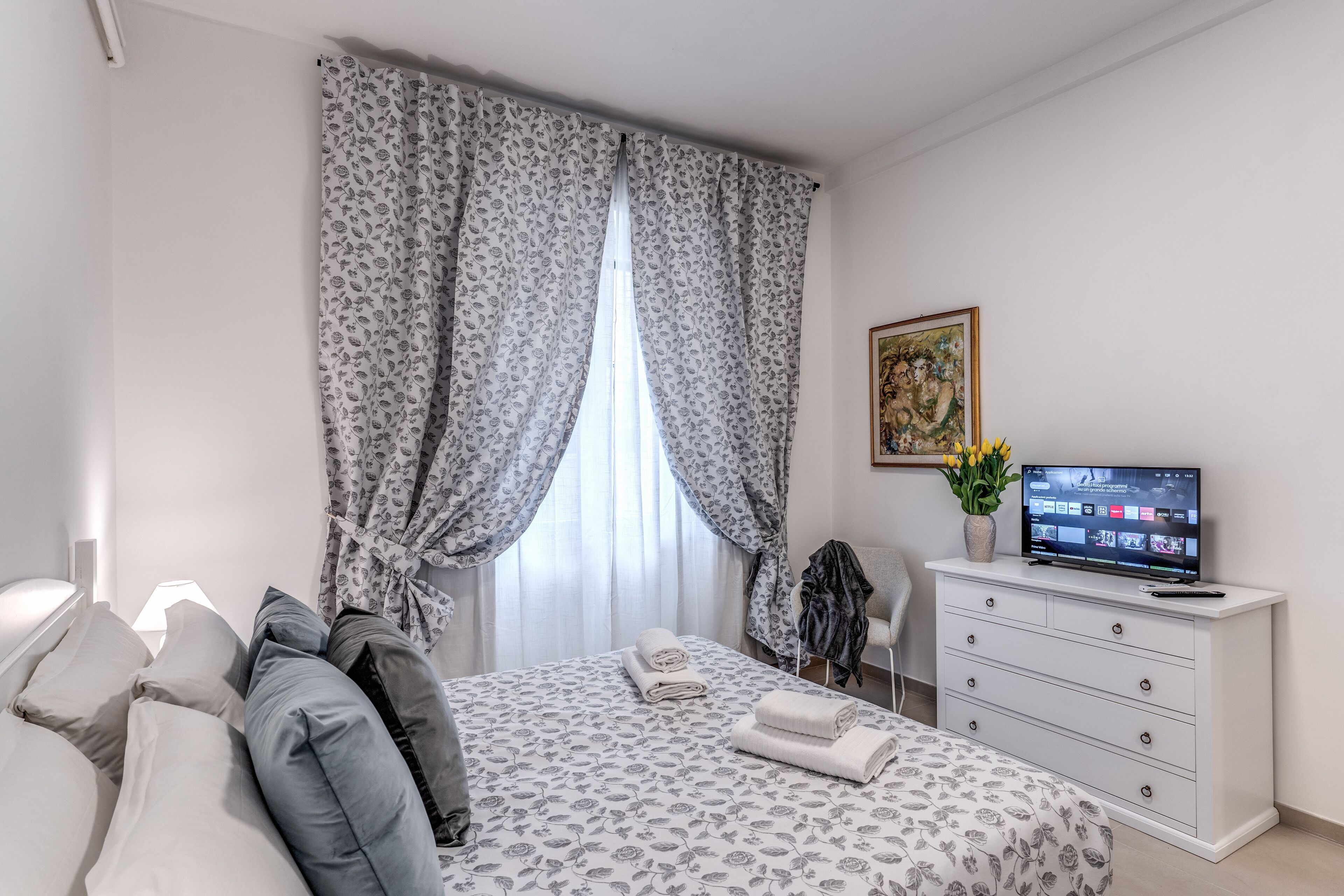 Un dormitorio ordenado con cama, mesita de noche y televisor sobre una cómoda.