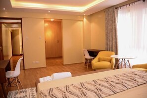A hotel room with a bed, a desk, a chair, a small table, and a television. - Lux Suites Westlands Penthouse (Nairobi)