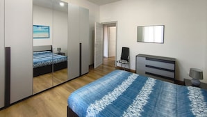 A modern bedroom with a large bed, a wardrobe, a desk, and a chair. - Calypso Holiday Home, cozy apartment in Station area for 5 Terre (La Spezia)