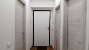 A narrow hallway with wooden flooring and white walls, leading to a door with a black frame. - Calypso Holiday Home, cozy apartment in Station area for 5 Terre (La Spezia)