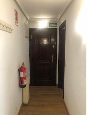 Leading to a secure exit, this hallway features a wooden floor and a fire extinguisher for added safety.