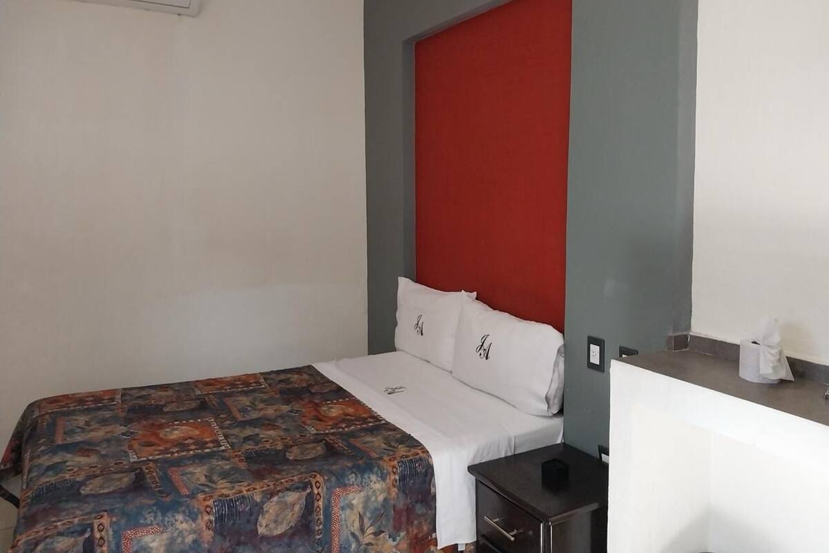 A hotel room with a bed, a red accent wall, a white ceiling, and a small desk with a tissue box.