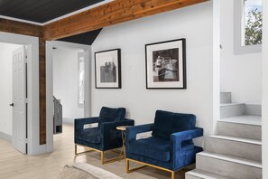 Un salon moderne avec deux fauteuils bleus en velours, une petite table ronde et un escalier menant à un niveau supérieur.