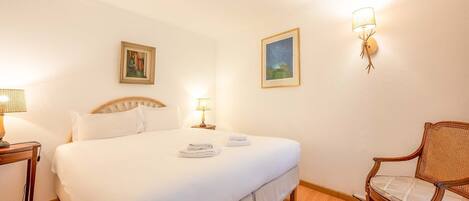 A hotel room with a large bed, two bedside lamps, a chair, and two framed pictures on the wall.