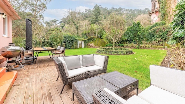 Een terras met rieten meubels, een barbecue en een verzorgde tuin.
