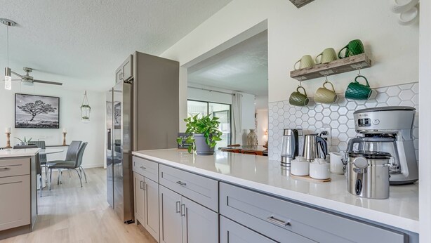 Una cocina moderna con encimera blanca, electrodomésticos de acero inoxidable y un comedor con mesa y sillas.