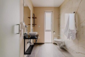 Features a large mirror, vessel sink, toilet, and towel rack in a minimalist bathroom.
