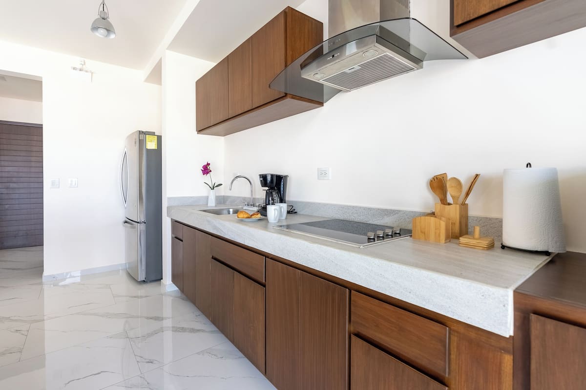 A modern kitchen with a marble countertop, wooden cabinets, a stainless steel range hood, and a built-in oven.