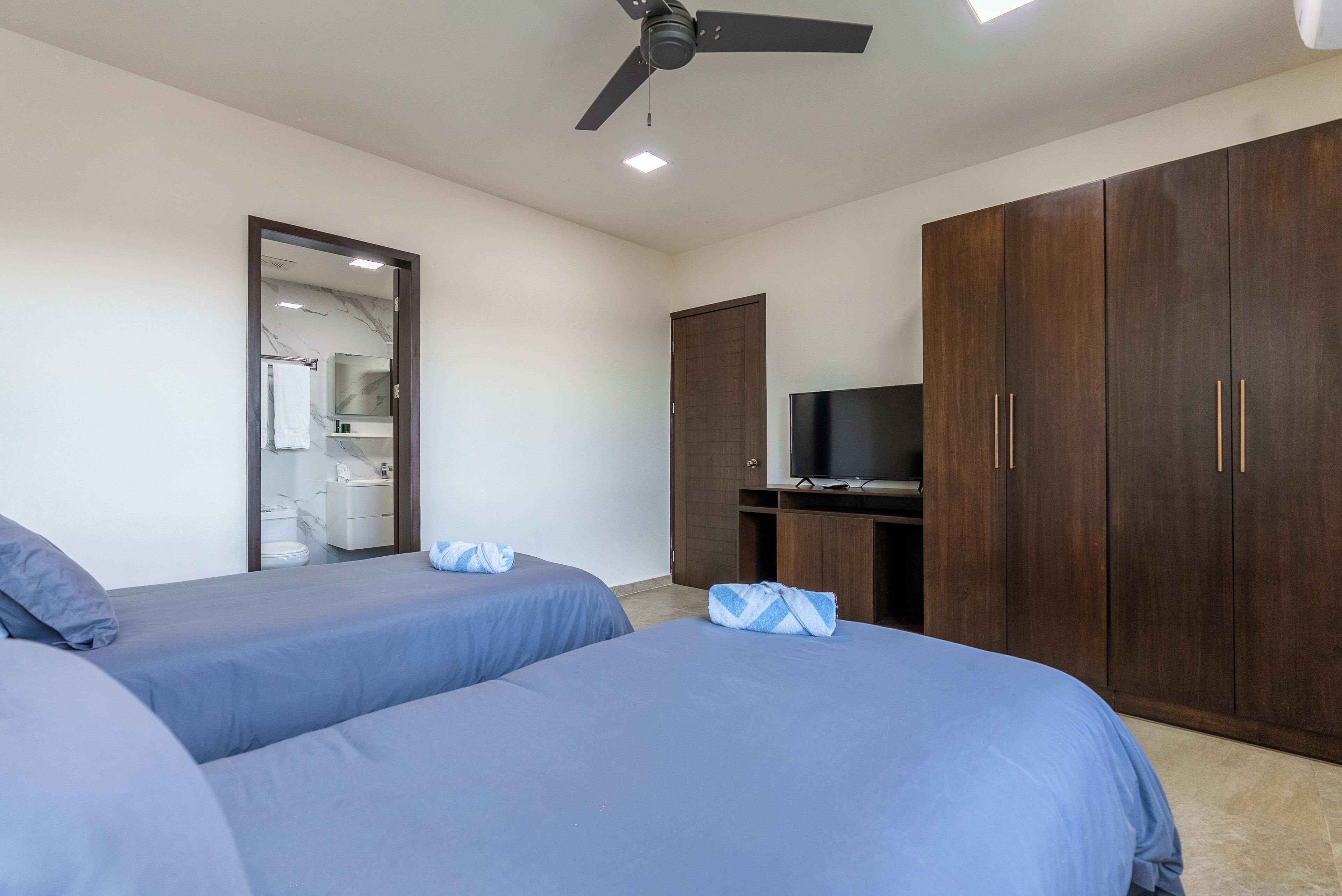 A hotel room with two beds, a ceiling fan, a TV, and a wardrobe.