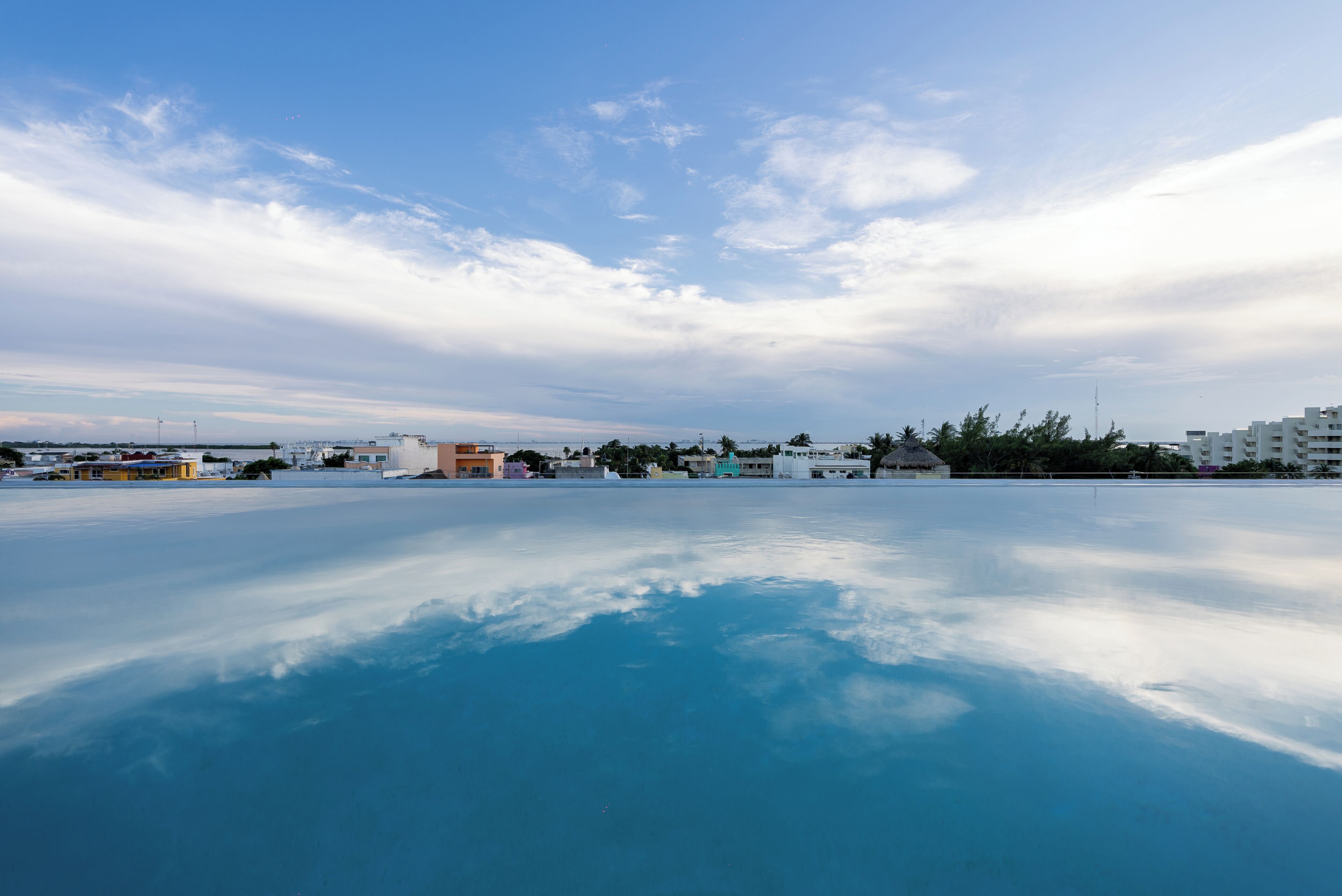 A clear sky with clouds, a calm body of water reflecting the sky, and buildings in the background.
