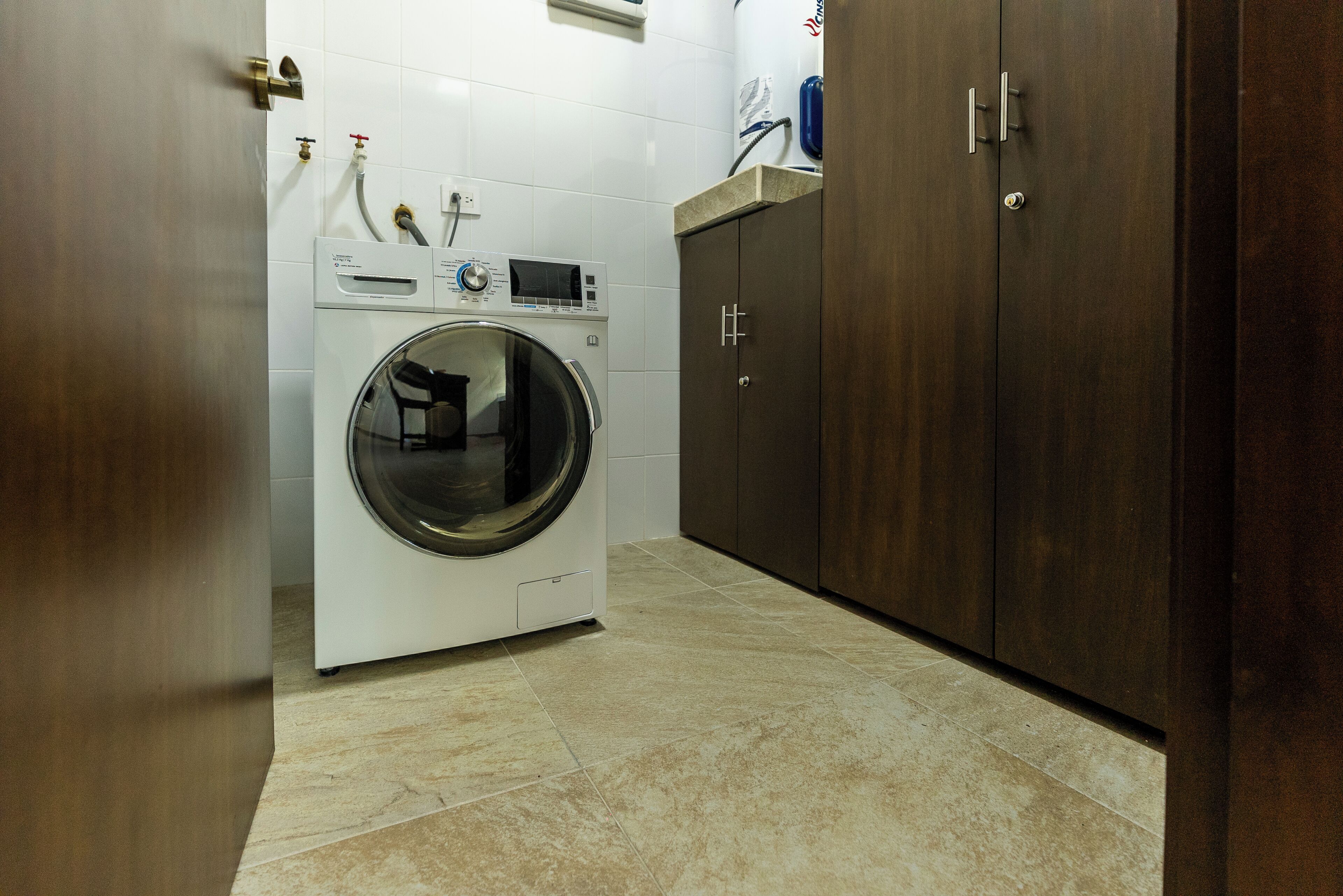 A laundry room with a front-loading washing machine, a cabinet, and a tiled floor.