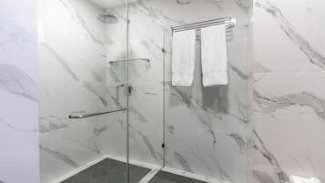 A modern bathroom with marble walls, a glass shower enclosure, and a towel rack.