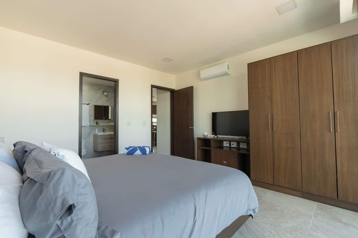 A bedroom with a bed, wardrobe, television, and an air conditioning unit.