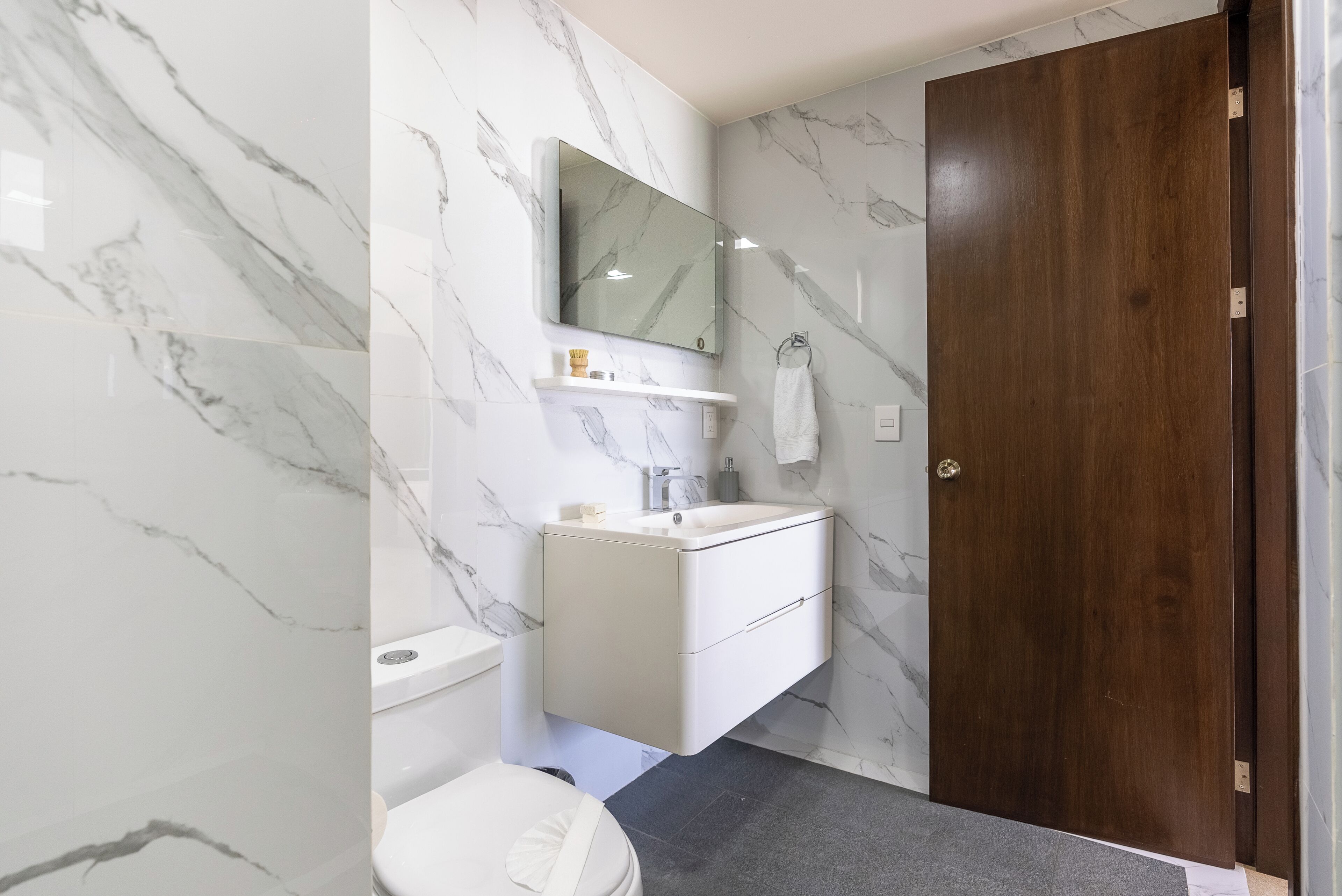 A bathroom with marble walls, a wooden door, a white sink, and a mirror above it.
