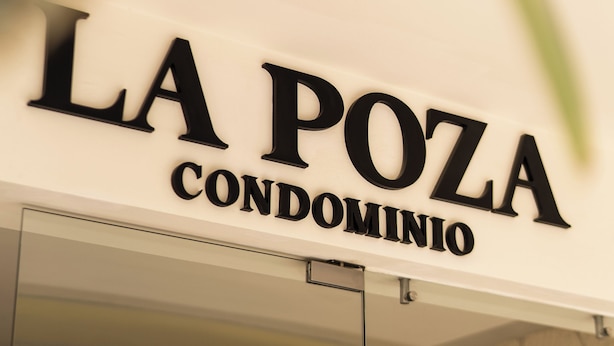A sign for 'LA POZA CONDOMINIO' with a glass entrance and a stone wall background. - La Poza (Isla Mujeres)