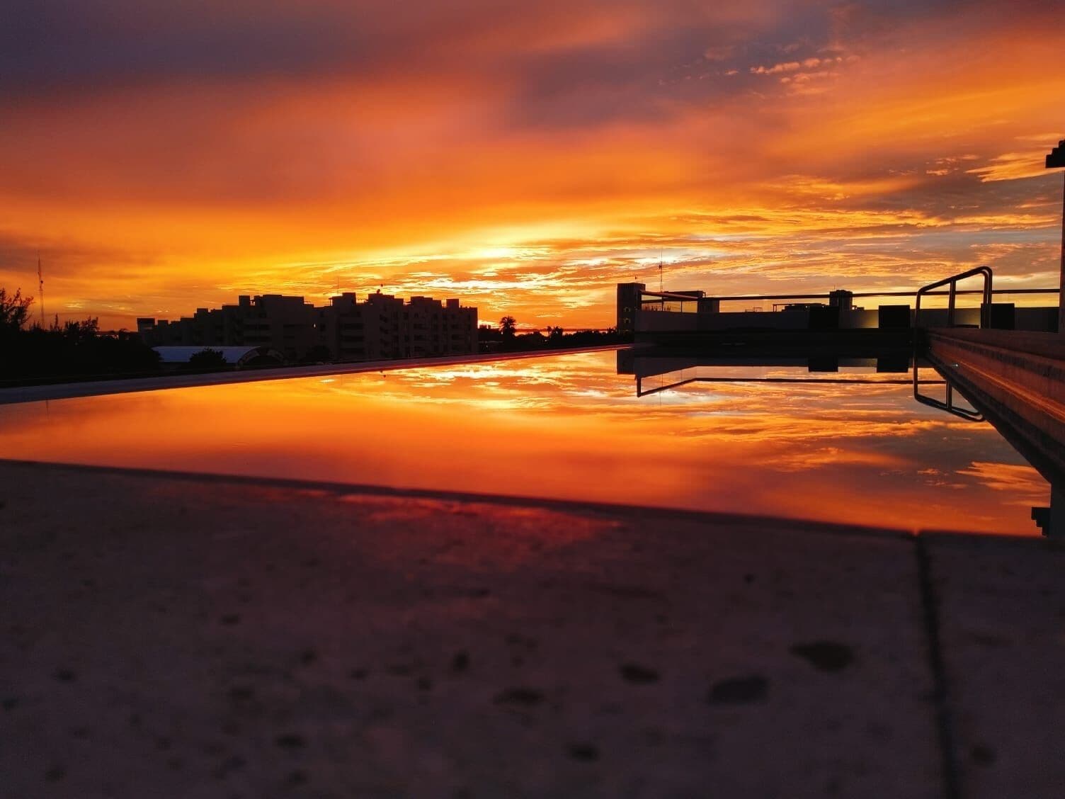 Un atardecer sobre una masa de agua, con un puente y edificios al fondo.