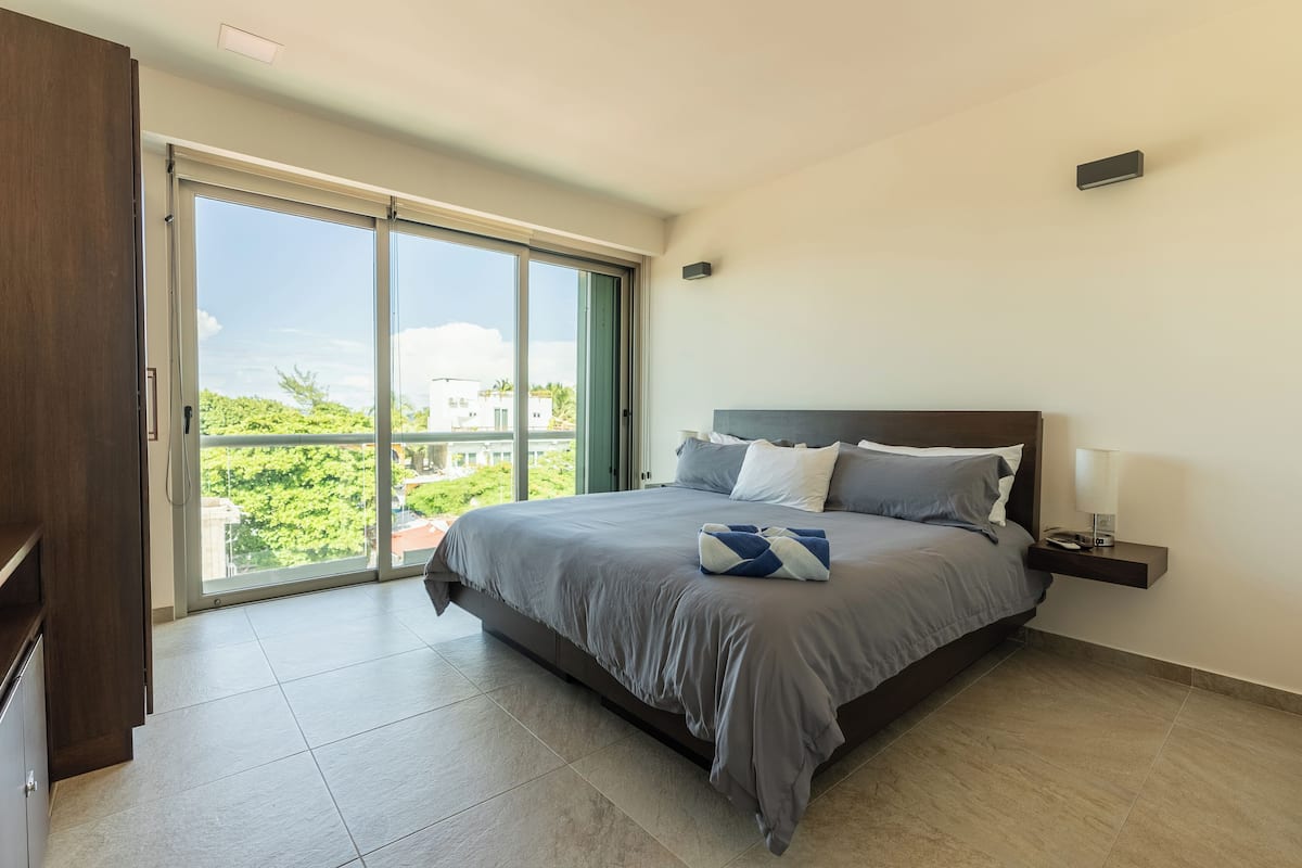 A bedroom with a large bed, a nightstand, a lamp, and a sliding glass door leading to a balcony.