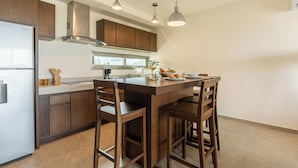 A modern kitchen with wooden cabinets, a stainless steel refrigerator, a built-in oven, and a large island with bar stools. - La Poza (Isla Mujeres)