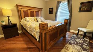 A bedroom with a wooden bed, a nightstand, a chair, and a window with curtains.