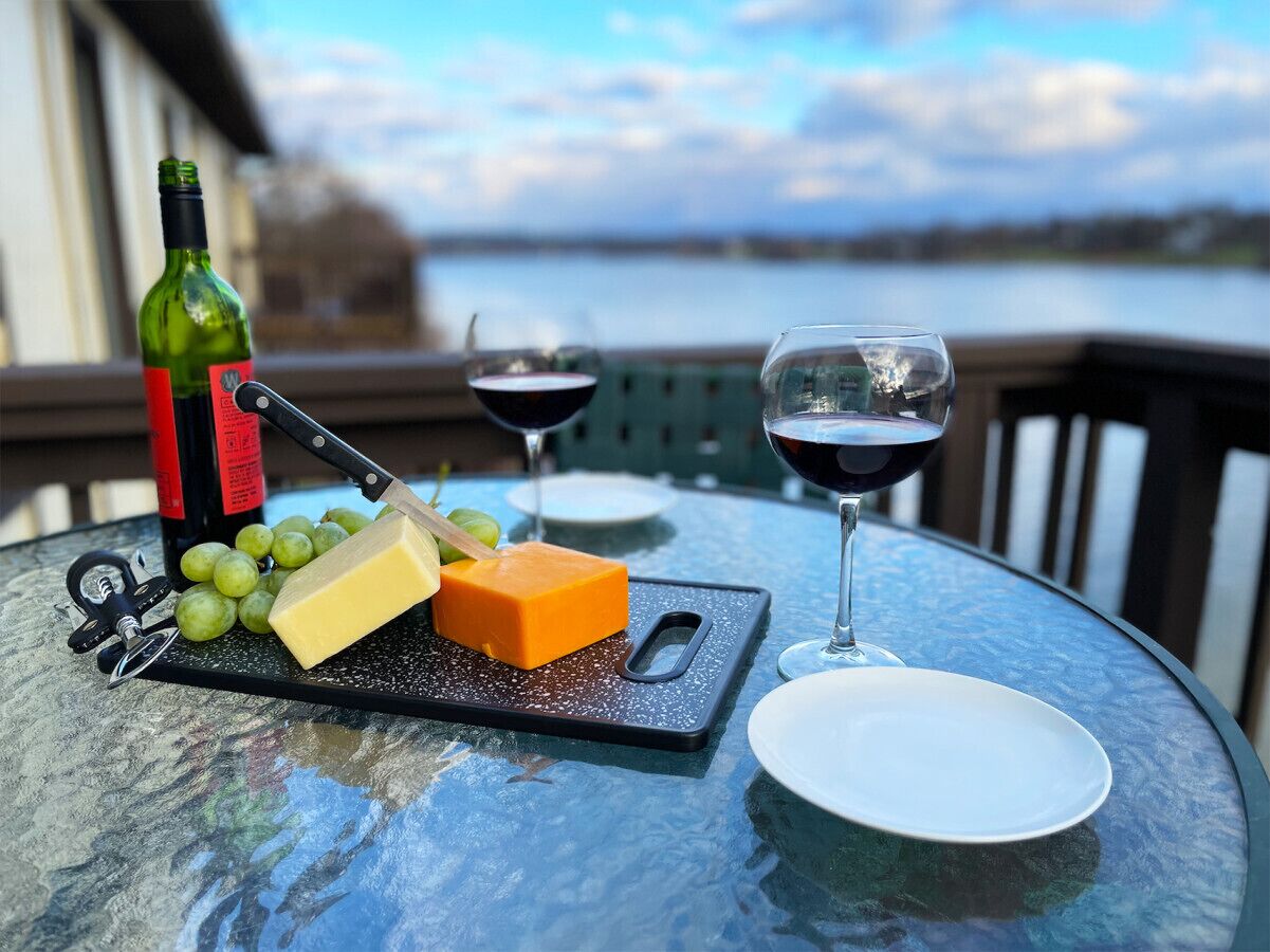 Une table dressée avec du fromage, des raisins, une bouteille et deux verres de vin rouge, le tout placé devant un paysage pittoresque.