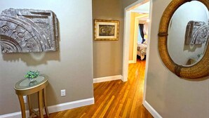 Un pasillo con piso de madera, un espejo redondo y una obra enmarcada en la pared.