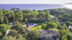 Vista aerea di una proprietà con piscina, vegetazione lussureggiante e vista mare.