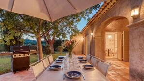 Un'area pranzo all'aperto con un tavolo imbandito per sei persone, un barbecue e un portico coperto.