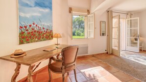 Una stanza con un tavolo di legno, una sedia, un quadro con fiori rossi, una finestra e una porta.