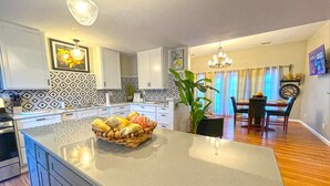 A modern kitchen with a central island, a dining area with a chandelier, and patterned backsplash tiles. - Captain's Quarters | One Bed Condo Waterfront on Ohio River (Marietta)