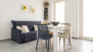 Ett modernt vardagsrum med en mörkblå soffa, två fåtöljer med detaljerade ryggstöd, ett vitt matbord med en grön skål och väggkonst som föreställer solrosor.