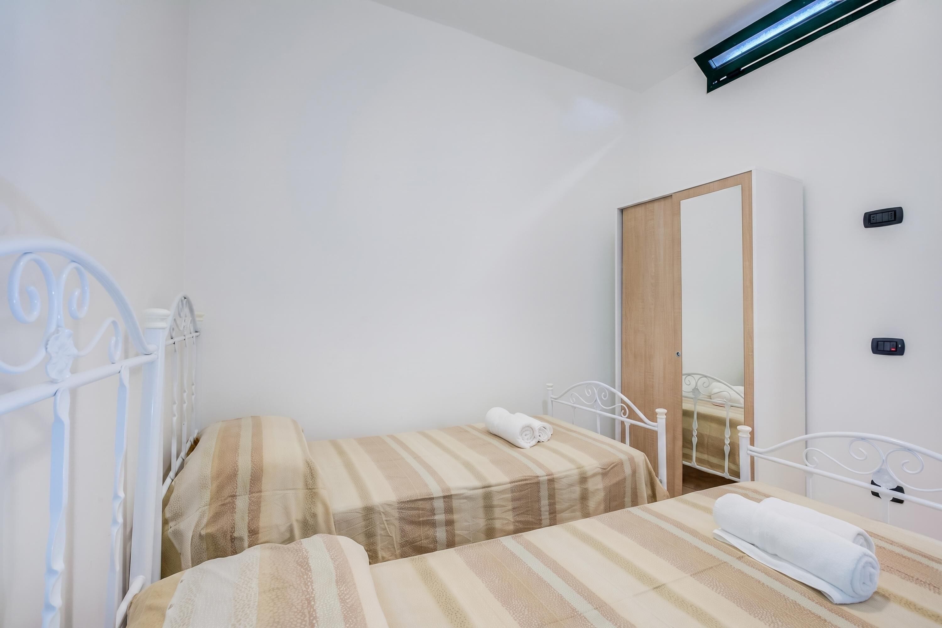 A bedroom with two beds, a mirror, and a ceiling light fixture.