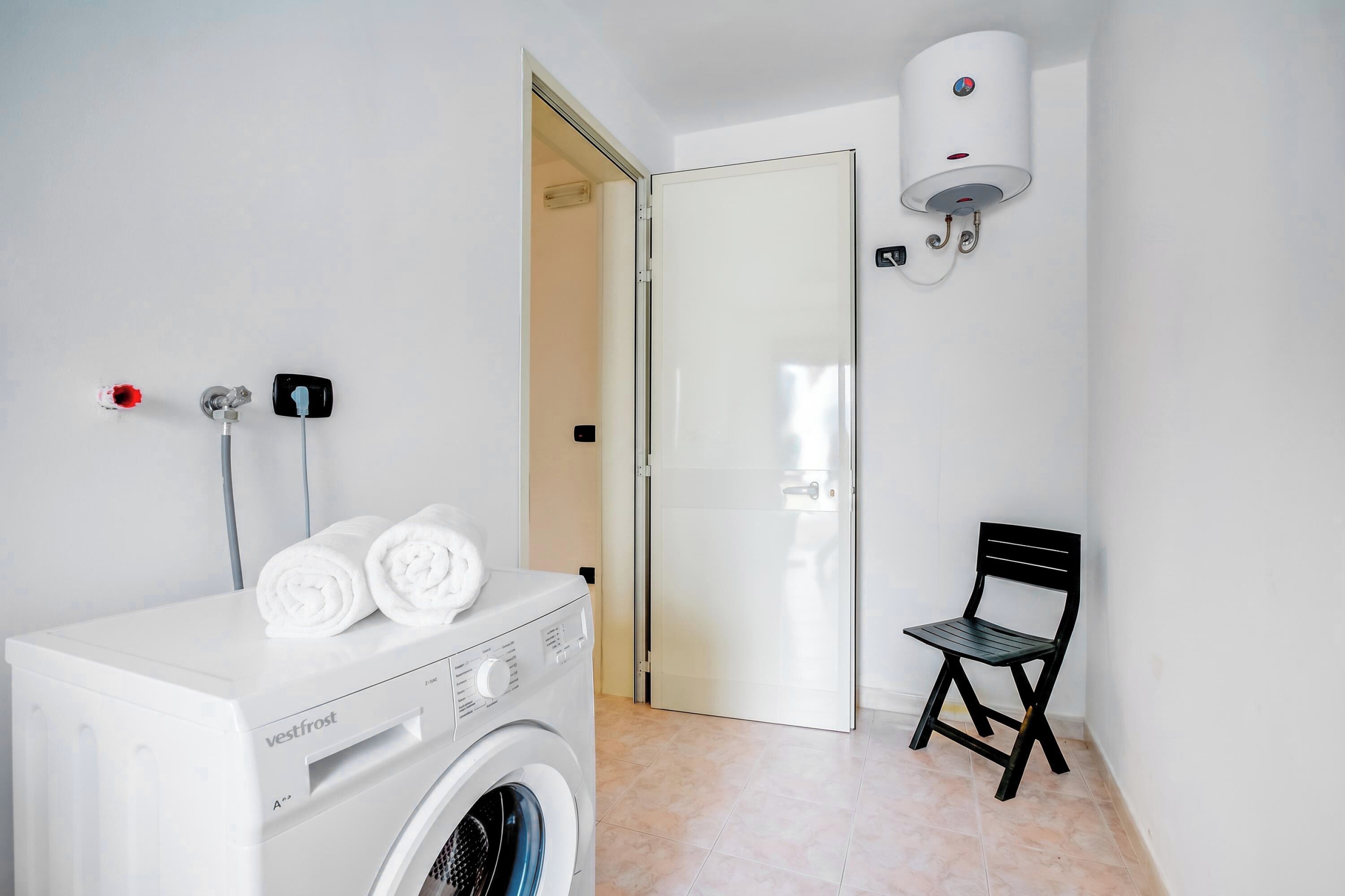 A laundry area with a white washing machine, a black chair, and a water heater on the wall.