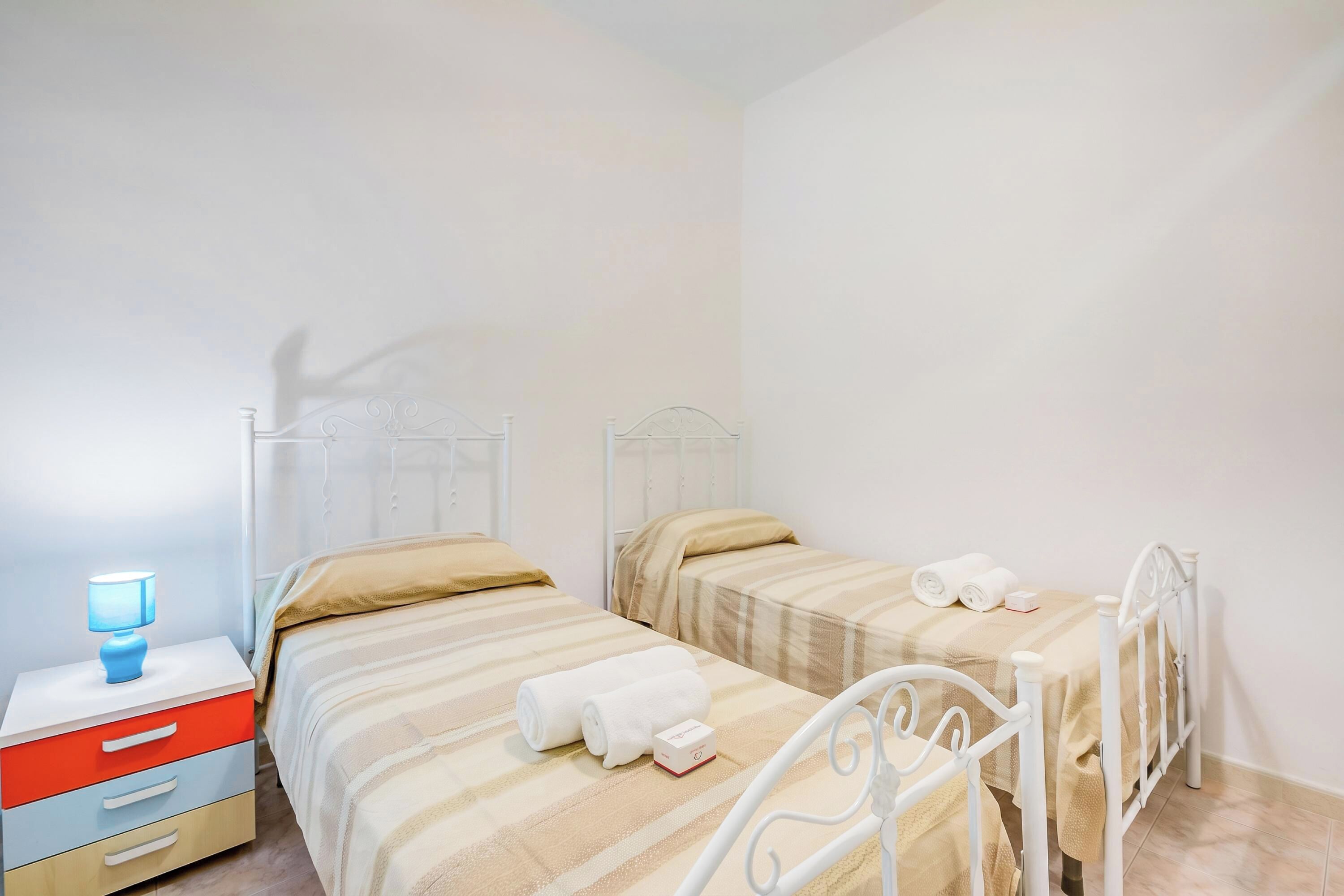 A bedroom with two beds, a nightstand with a lamp, and a red drawer.