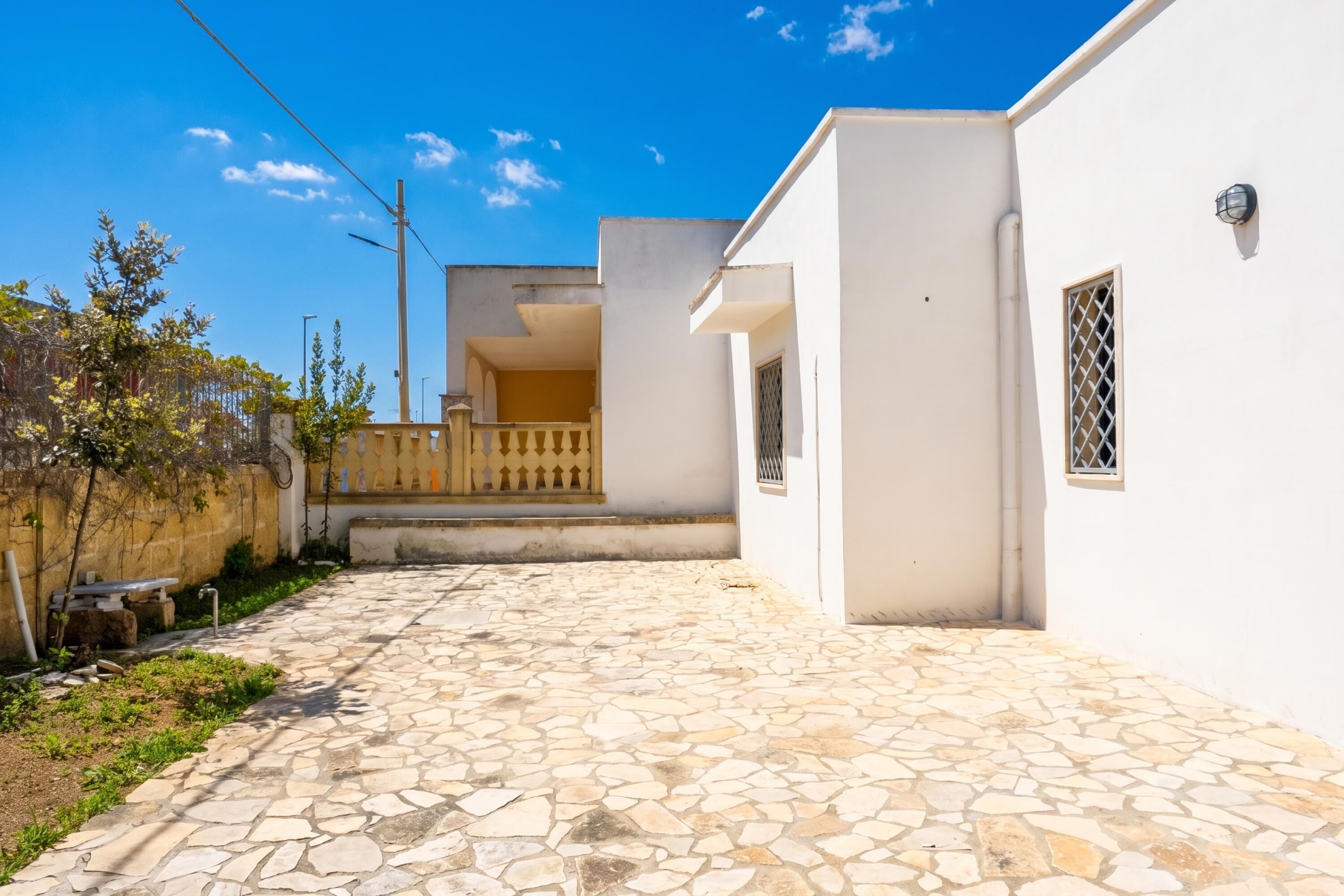 A courtyard with a stone floor, white walls, and a balcony.
